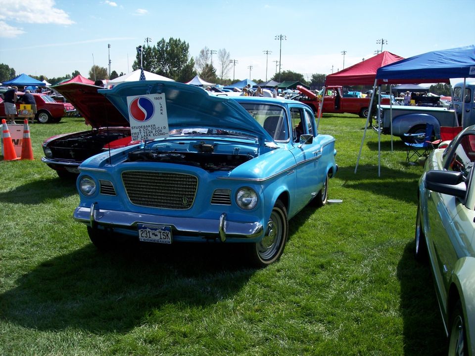 Blue 1959 Studebaker Lark with hood open, parked on grass at an outdoor car show