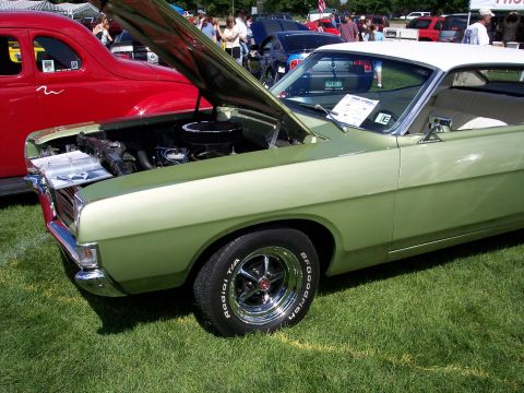 1972 Ford Ranchero - A light green coupe with a white roof and hood open is displayed on a grassy field, with other vehicles and people in the background.