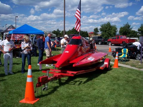 1972 Ford Ranchero - A bright red, low-profile race boat is displayed on a trailer at an outdoor event.