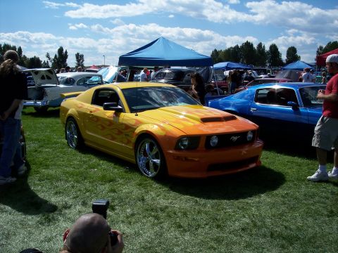 1972 Ford Ranchero - A custom Ford Mustang with flame decals and a hood scoop is displayed at an outdoor car show.