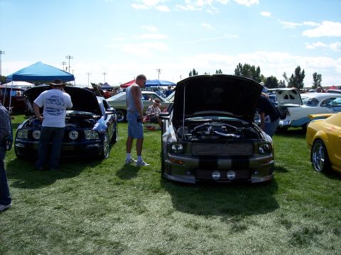 1972 Ford Ranchero - Car show attendees examine a grey Ford Mustang GT with its hood open, next to a dark blue Mustang.