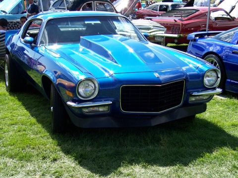 1972 Ford Ranchero - A bright blue muscle car with a prominent hood scoop is displayed on a grassy field alongside other vehicles.