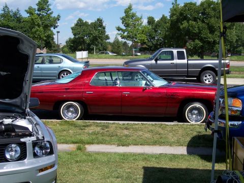 1972 Ford Ranchero - A shiny red sedan with whitewall tires and wire wheels is parked on the side of the road, with other vehicles visible in the background.