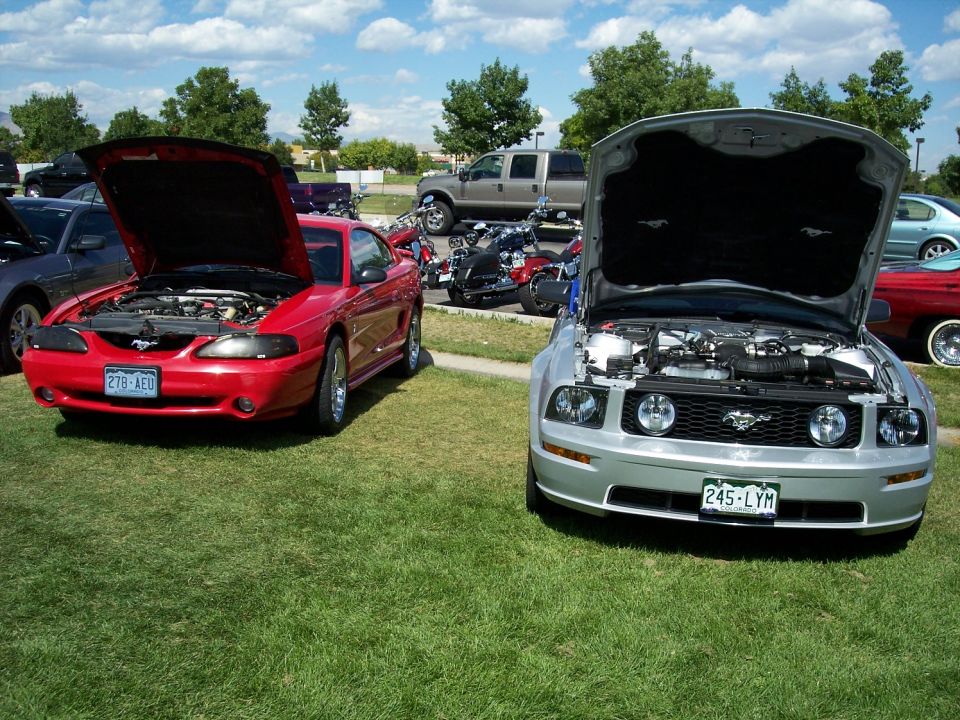 Silver 2005 Ford Mustang front view, hood open. Red 1994-1998 Ford Mustang front view, hood open, parked to the left