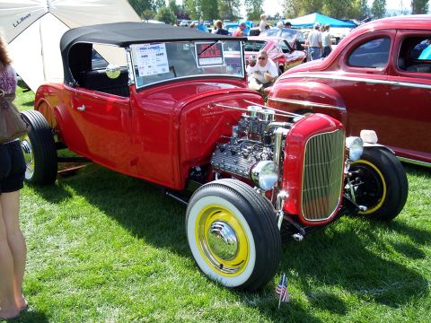 1972 Ford Ranchero - A bright red hot rod convertible is parked on grass next to another red vehicle at an outdoor car show.
