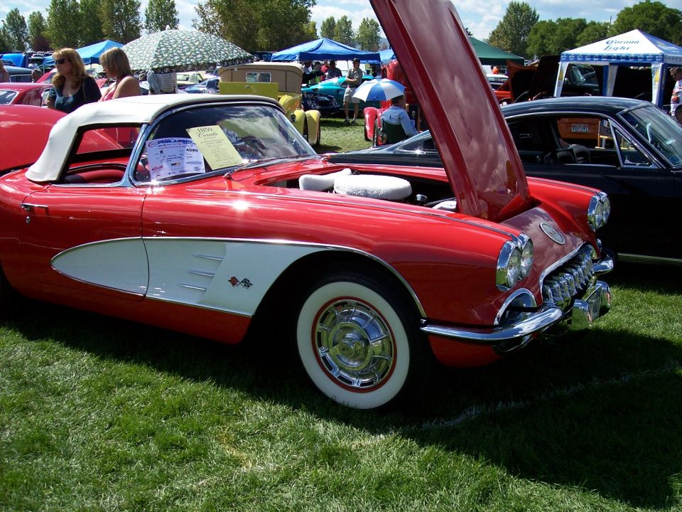 Red 1958 Chevrolet Corvette convertible with white coves and a white soft top, hood open, parked on grass