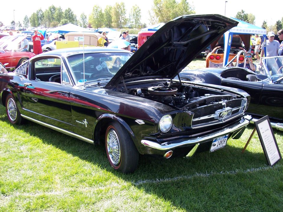 Black 1965 Ford Mustang coupe with hood open, wire wheels, and red tire accents