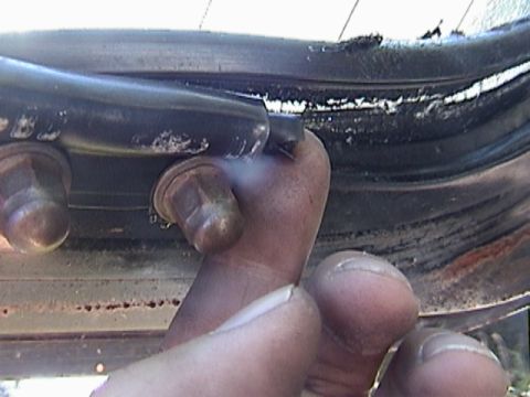 1977 Ford Mustang - A close-up shot focuses on a person's fingers interacting with a worn door seal and exposed bolts on a vehicle.