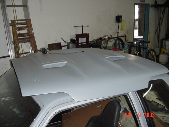 Gray primered hood with twin scoops resting on a car roof in a workshop
