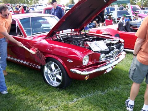 1972 Ford Ranchero - A red 1965 Ford Mustang is being detailed at an outdoor car show, with its hood open to reveal the engine.