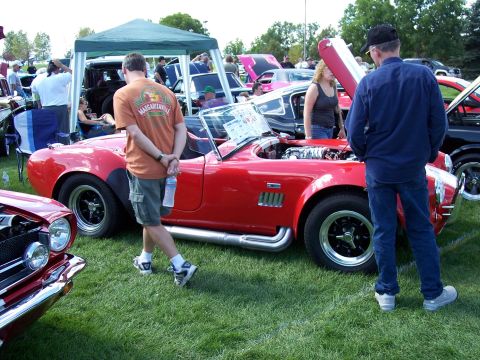 1972 Ford Ranchero - People gather around a red convertible sports car with its hood open at an outdoor car show.