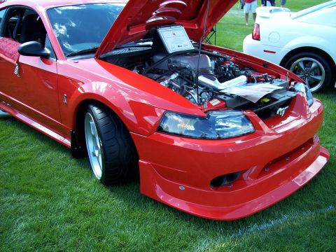 1972 Ford Ranchero - A red Ford Mustang is displayed with its hood up, revealing the engine, while another white Mustang sits nearby on a grassy field.