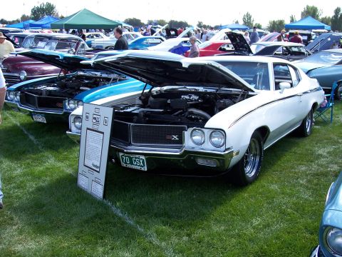 1972 Ford Ranchero - A white 1970 Buick GSX is displayed with its hood open at an outdoor car show.