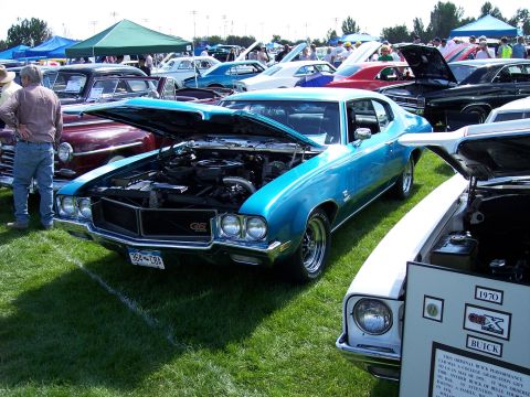 1972 Ford Ranchero - A blue muscle car is displayed with its hood open at an outdoor car show, with other vehicles and tents in the background.