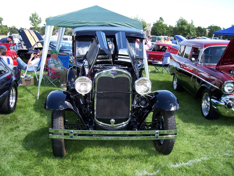 Front view of a black 1930s car with hood open, parked on grass