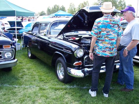 1972 Ford Ranchero - Two men look at a black 1955 Chevrolet sedan with its hood open at an outdoor car show.