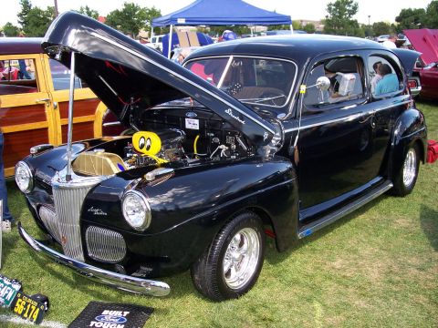 1972 Ford Ranchero - A classic black Ford sedan is displayed with its hood up, revealing the engine bay at an outdoor car show.