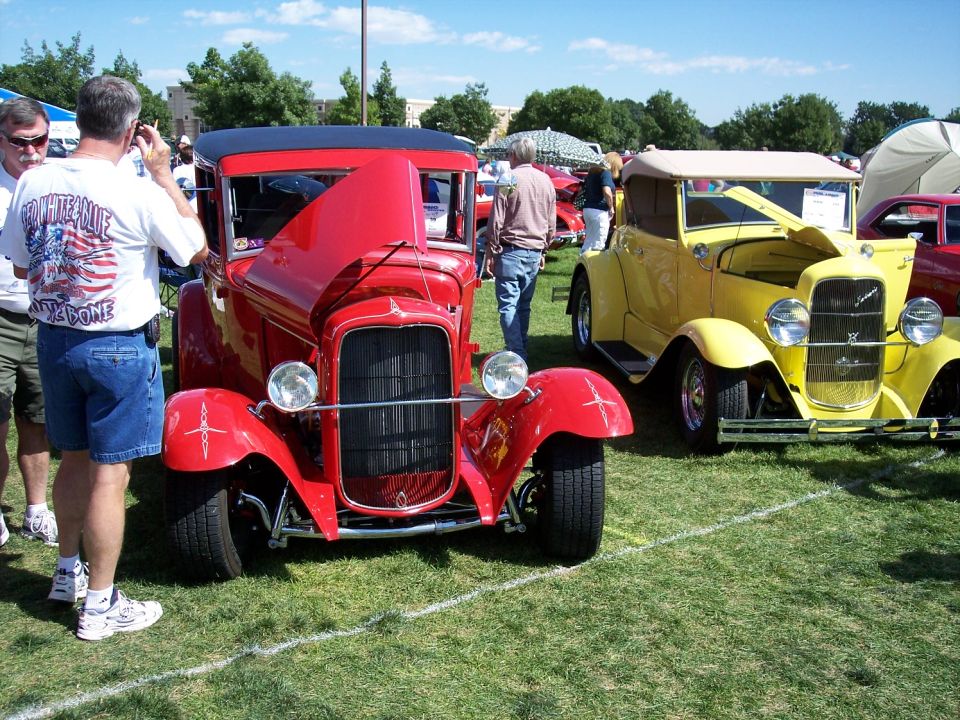 Red hot rod with hood open, parked on grass next to a yellow car