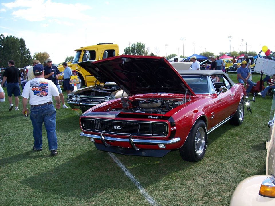 Red 1967 Chevrolet Camaro SS convertible with hood open. Yellow truck and other cars in background