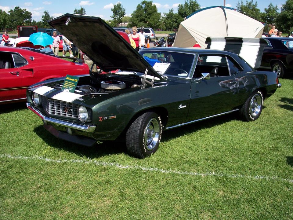 Green 1969 Camaro Z/28 with hood open, white stripes on hood, parked on grass next to a red car
