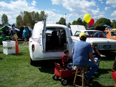 1972 Ford Ranchero - A white panel van with custom flame decals is displayed at an outdoor event with people gathered around.
