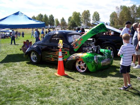 1972 Ford Ranchero - A custom hot rod coupe with flame graphics and an exposed engine is displayed at an outdoor car show.