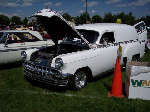 1972 Ford Ranchero - A white panel van, possibly a 1950s Chevrolet, is displayed with its hood open at a car show. The vehicle features chrome accents and flame…