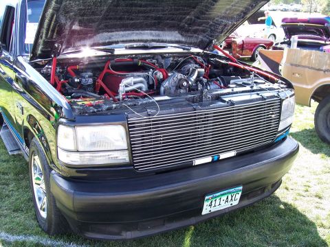 1972 Ford Ranchero - A modified engine bay of a Ford F-Series truck is displayed at an outdoor car show with other vehicles present.