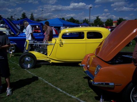 1972 Ford Ranchero - A yellow hot rod sedan is parked on a grassy field next to other vehicles.