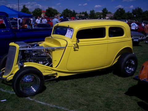 1972 Ford Ranchero - A bright yellow hot rod coupe is displayed at an outdoor car show, with other vehicles and tents in the background.