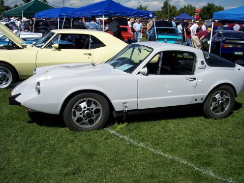 1972 Ford Ranchero - A white sports car is displayed on a grassy field at an outdoor event with other vehicles present.