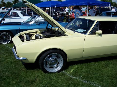 1972 Ford Ranchero - A pale yellow 1967 Chevrolet Camaro coupe is displayed with its hood open at an outdoor car show.