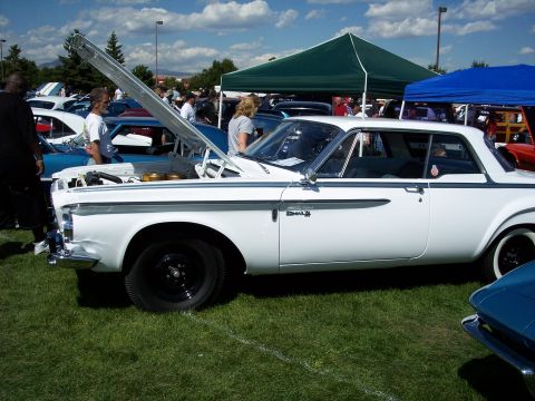 1972 Ford Ranchero - A white 1962 Dodge Lancer coupe is displayed with its hood open at an outdoor car show.
