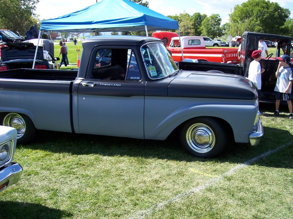 Gray and black Ford F-100 pickup truck with custom wheels parked on grass