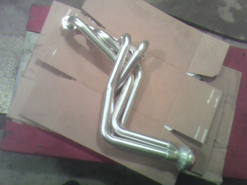 Shiny metal exhaust headers on cardboard