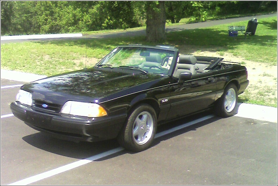 Black convertible with a gray interior parked on asphalt. The "5.0" badge is visible on the fender
