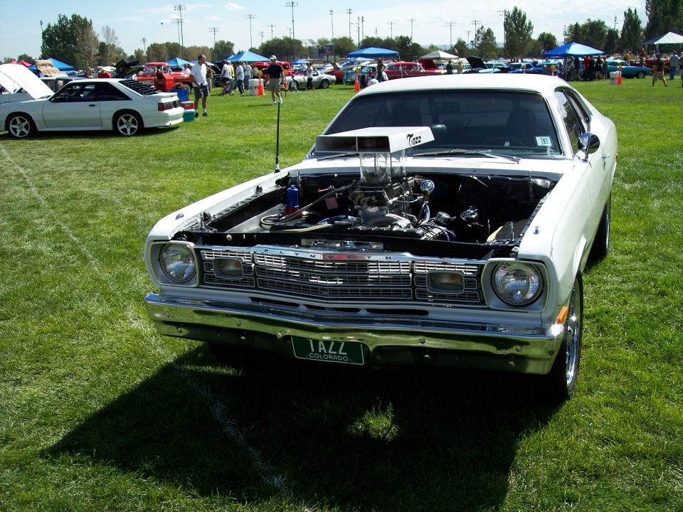 White Plymouth Duster with hood open, showing engine and scoop. License plate reads 'IAZZ COLORADO'. Another white car is parked nearby