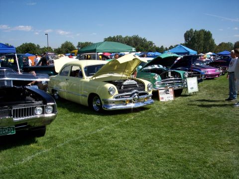 1972 Ford Ranchero - A yellow 1950s sedan is displayed with its hood open at an outdoor car show.