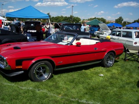 1972 Ford Ranchero - A red convertible is displayed at an outdoor car show with other vehicles and tents in the background.