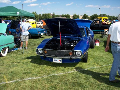 1972 Ford Ranchero - Blue AMC AMX at a car show, hood open to display the engine. Other vehicles are parked on the grass.