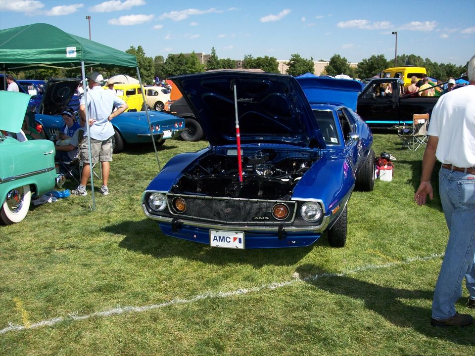 Blue AMC AMX coupe with hood open at grass car show, AMX grille badge and AMC front plate