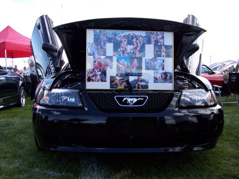 1972 Ford Ranchero - A black car with its hood and doors open displays a collage of photographs on its grille, with another vehicle visible in the background.