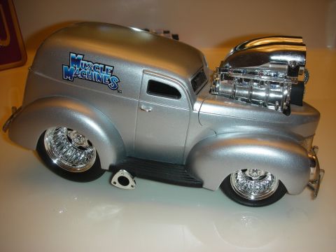 1998 Ford Crown Victoria - silver Muscle Machines diecast panel-delivery hot rod with a chrome blown engine sticking through the hood, side view.