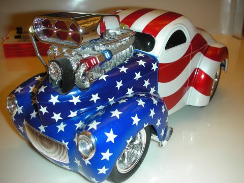 1998 Ford Crown Victoria - diecast coupe hot rod painted with stars and stripes and a chrome blown engine, posed front-quarter on a glossy surface.