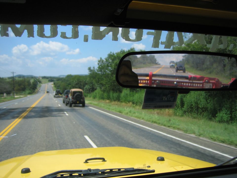 Yellow Jeep interior view of road with other Jeeps ahead; TX Tag visible