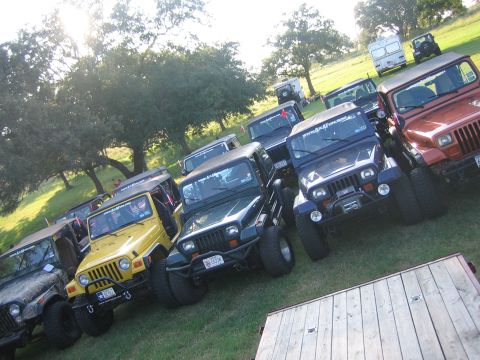 2001 Jeep Wrangler - A group of Jeep Wranglers are parked together on a grassy field, with trees and a trailer in the background.