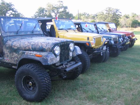 2001 Jeep Wrangler - Multiple Jeeps are lined up on a grassy field, with the closest vehicle a camouflage wrap and a website address on its windshield.