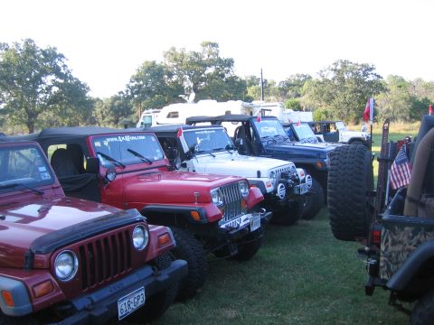 2001 Jeep Wrangler - Multiple Jeep Wranglers are lined up on a grassy field, with trees and RVs visible behind them.