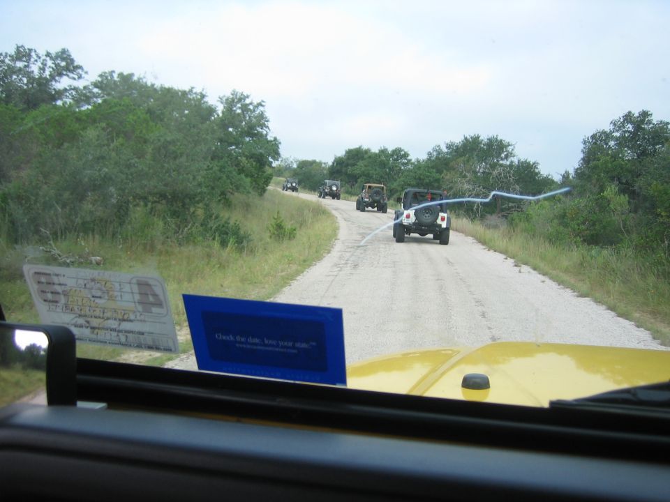 Yellow Jeep hood in foreground, convoy of Jeeps on dirt road ahead