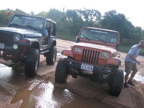 2001 Jeep Wrangler - Two Jeep Wranglers are parked on a wet dirt road, with a person walking behind the orange one.
